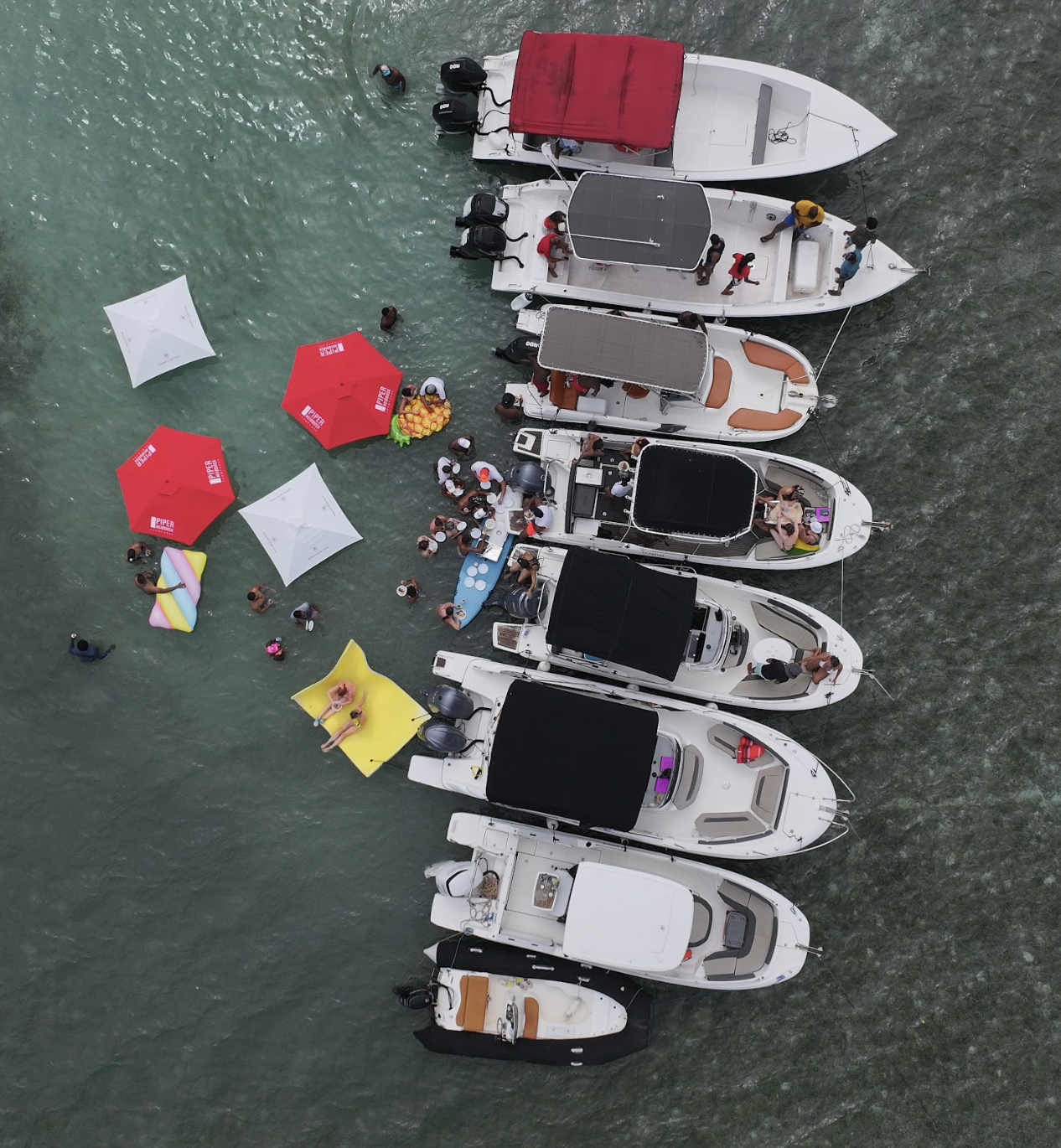 Vue aérienne de plusieurs bateaux amarrés en Martinique, entourés de participants dans l’eau turquoise lors d’une Boat Party ONE PEACE FWI, avec bouées colorées et parasols sur la mer des Caraïbes.